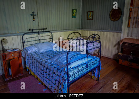 CHILOE, CHILE - SEPTEMBER, 27, 2018: Indoor view of metallic bed with two wooden pedestal table inside of Chonchi museum, donated by families of Chonchi, opened in 1996 Stock Photo