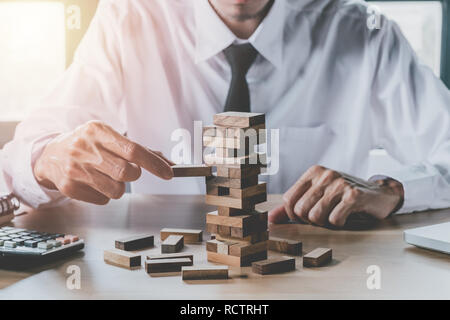 Hand of businessman pulling out or placing wood block on the tower in modern office. Risk and strategy in business. Stock Photo