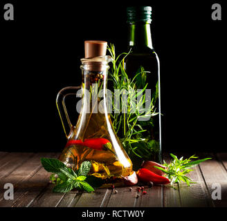 Bottles with oil, herbs and spices at wooden table on black background Stock Photo