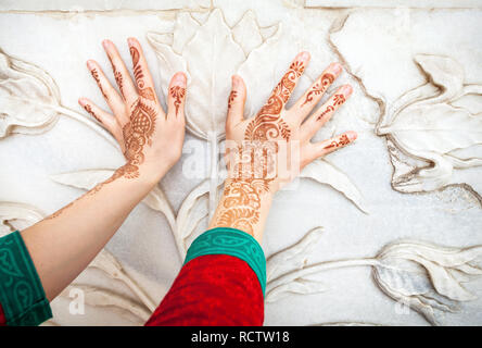 Woman in red Indian costume touching white marble wall with floral pattern by hands in henna painting in Taj Mahal in Agra, Uttar Pradesh, India Stock Photo