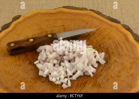 Chopped shallot onion with kitchen knife on cutting board made from tree trunk Stock Photo