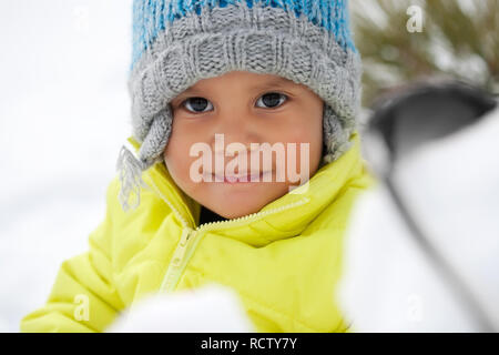 Cute Latino toddler smiling while playing in the snow during winter and wearing a knit hat. Stock Photo