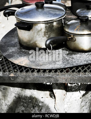 Close up of aluminum pots and pans with lids cooking outside on a fire pit Stock Photo