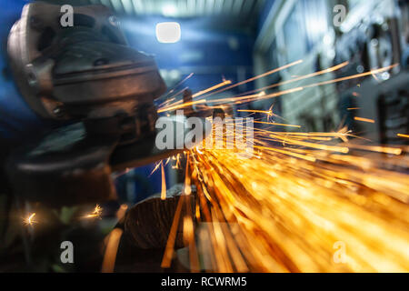A close-up of a car mechanic using a metal grinder to cut   bearing in an auto repair shop, bright flashes flying in different directions. Work of aut Stock Photo