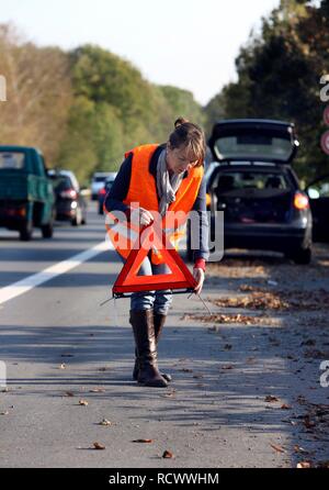 Car breakdown, female driver has stopped on the hard shoulder of a country road, wearing a reflective vest Stock Photo