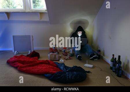 Hacker working on a laptop computer in a sparsely furnished apartment, symbolic image for computer hacking, computer crime Stock Photo