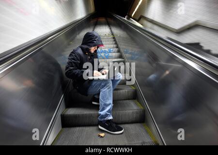 Hacker working on a laptop computer on an escalator in a subway passage at night, symbolic image for computer hacking Stock Photo