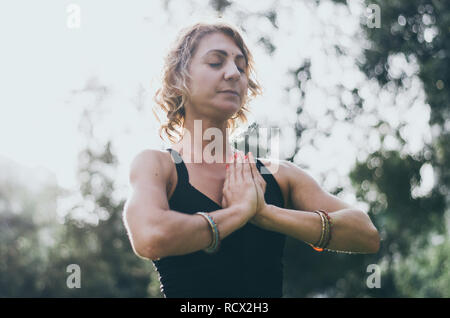Beautiful young woman meditates in yoga asana Padmasana - Lotus pose on the wooden deck in the autumn park. Stock Photo