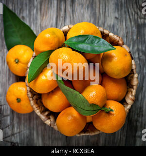 Tangerines with leaves in basket on rustic wooden background. Stock Photo