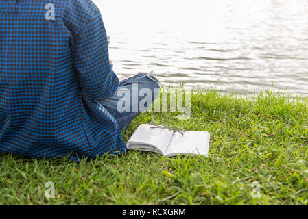 Woman sitting beside opened book and glasses on grass Stock Photo