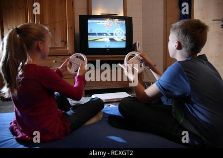 Siblings, a boy, 12 years old, and a girl, 10 years old, playing a car racing game on a Wii games console in their room together Stock Photo