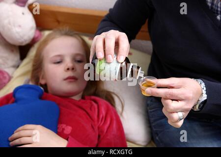 Girl, 10 years old, is ill in bed with a cold, flu, fever, cough, her mother is giving her cough syrup Stock Photo