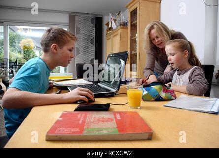 Siblings doing their homework in the living room, their mother is helping them Stock Photo