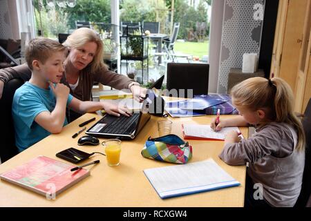 Siblings doing their homework in the living room, their mother is helping them Stock Photo