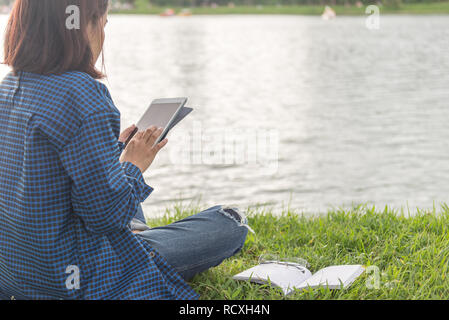 Woman sitting beside a lake and using tablet Stock Photo