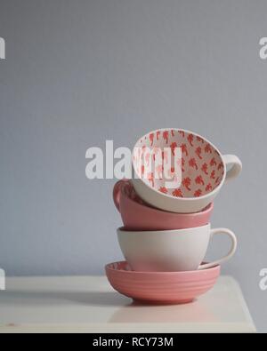 Close up of coral pink and white tea cups stacked on white table. Cups decorated with palm tree pattern. Pantone Color of the Year 2019 - Living Coral. Stock Photo