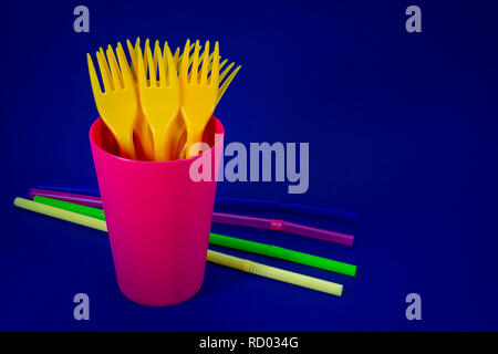 A pile of yellow plastic forks in a plastic pink mug and colored straws on blue background Stock Photo