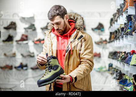 Man in winter jacket choosing trail shoes for mountain hiking in the sports shop Stock Photo
