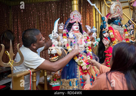 Two devout Hindu worshippers decorate a statue of the goddess Durga with flowers. In Ozone Park, Queens, New York. Stock Photo