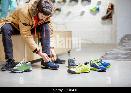 Man in winter jacket trying shoes for mountain hiking sitting in the fitting room of the modern sports shop Stock Photo