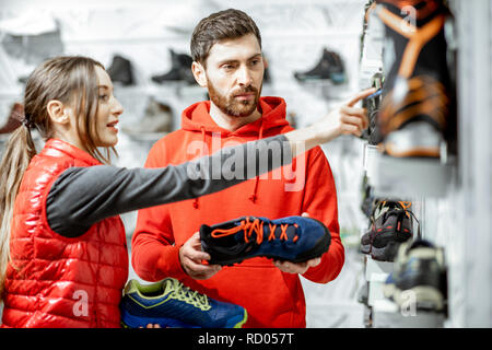 Mam and woman in red sports clothes choosing trail shoes for hiking standing near the showacase of the modern sports shop Stock Photo