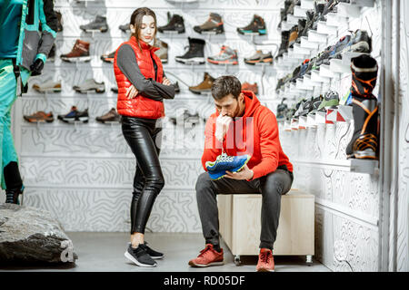 Man and woman choosing shoes for hiking sitting in the fitting room of the modern sports shop Stock Photo