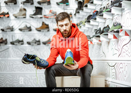 Man choosing trail shoes for hiking sitting in the fitting room of the modern sports shop Stock Photo