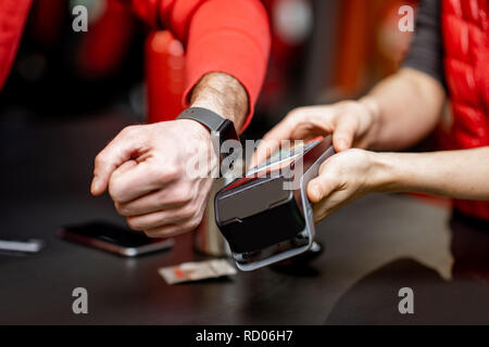 Man using handwatch on the cash register for buying goods at the sports shop, close-up view with no face Stock Photo