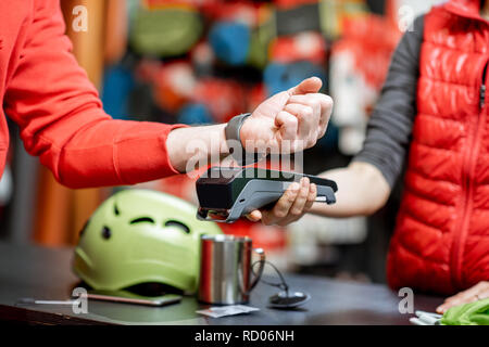 Man using handwatch on the cash register for buying goods at the sports shop, close-up view with no face Stock Photo