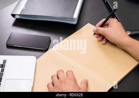 Overhead view of office table with mans hands writing to do list with pen on vintage notebook, computer keyboard, tablet pc and smartphone. copy space Stock Photo