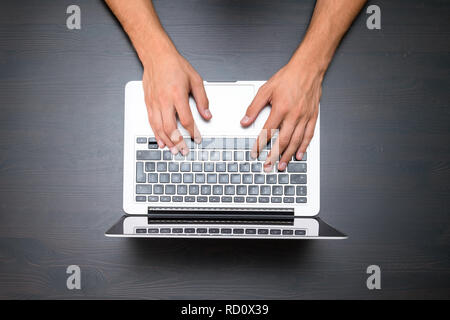 A man is working by using a laptop computer on vintage wooden table. Hands typing on a keyboard. Top view, business office workplace Stock Photo
