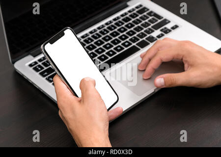 Mans hands typing on smart phone while working on laptop computer on vintage wooden table. Hands typing on a keyboard. Top view, business office work Stock Photo