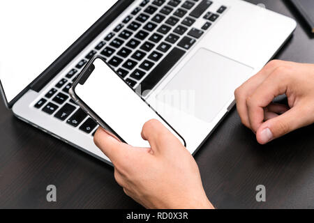 Mans hands typing on smart phone while working on laptop computer on vintage wooden table. Hands typing on a keyboard. Top view, business office work Stock Photo
