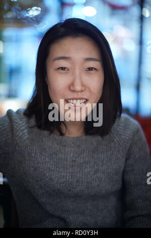 A friendly young Chinese woman with long hair is sitting in a bar smiling directly at the camera. Stock Photo