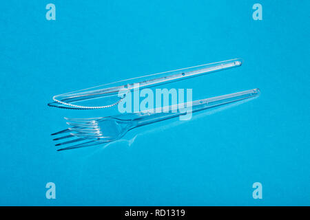 Plastic transparent fork and knife on blue background. Stock Photo