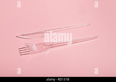 Plastic transparent fork and knife on pink background. Stock Photo