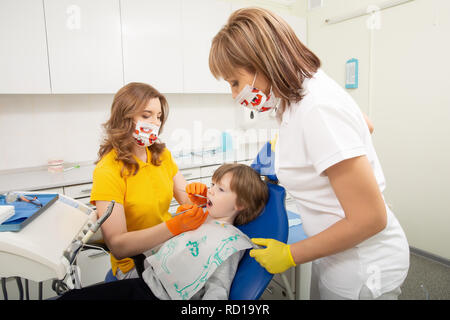 Dentist examining boy's teeth in clinic. A small patient in the dental chair smiles. Dantist treats teeth Stock Photo