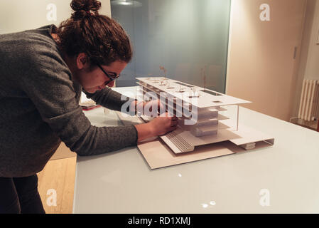 Female architect working on architecture model made with cardboard on table in office of architectural firm Stock Photo
