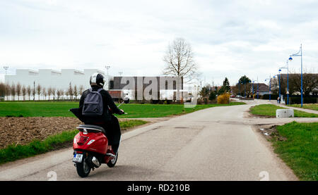 STRASBOURG, FRANCE - APR 2, 2018: Young carefree woman riding Italian Vespa Primavera 5 red scooter on a countryside road near Strasbourg  Stock Photo