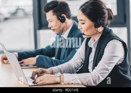 side view of young call center operators in headsets using laptops at workplace Stock Photo