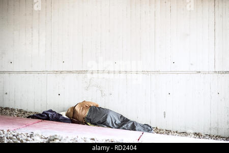 A rear view of homeless beggar man lying on the ground outdoors in city, sleeping. Stock Photo