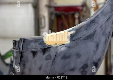 Detail of the iron damaged car bumper is repaired in the workshop using putty and grouting, prepared for sanding and painting. Stock Photo