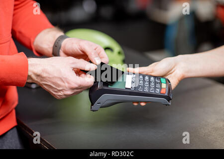 Man making purchase with bank card and cash register at the counter of the sports shop, close-up view Stock Photo