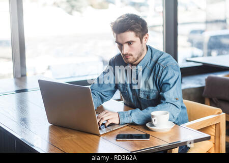 Portrait of young successful serious bearded businessman working on computer sitting in office. thoughtful entrepreneur connecting to wireless via com Stock Photo