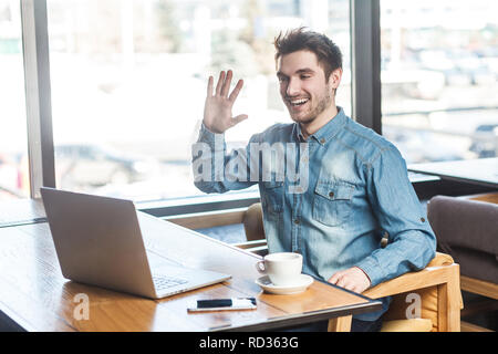 Give me five! Portrait of satisfied happy young businessman in blue jeans shirt are sitting in cafe and greeting a worker through a webcam and showing Stock Photo