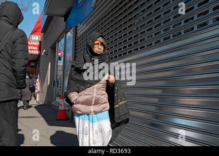 An older Muslim woman wearing a winter coat and niqab walking on 74th Street in Jackson Heights, Queens, New York City. Stock Photo