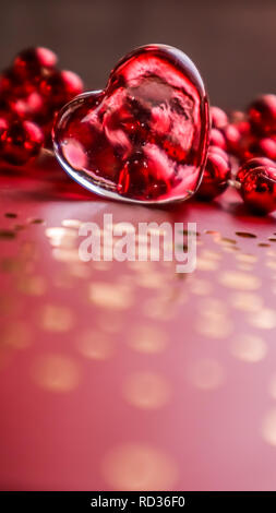 Shining transparent heart and red beads. Perfect Valentine's Day greeting card background. Vertical image in red tone Stock Photo