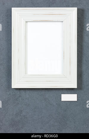 White wooden frame on grey painted wall, picture area isolated with clipping path. Blank caption plate and copy space below Stock Photo