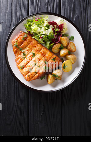 Healthy lunch grilled swordfish fillet with fried potatoes and fresh salad close-up on a plate on a wooden table. Vertical top view from above Stock Photo