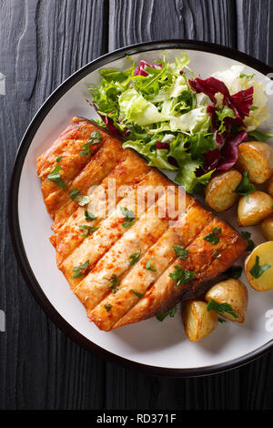 Grilled swordfish fillet with fried potatoes and fresh salad close-up on a plate on a wooden table. Vertical top view from above Stock Photo